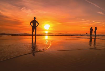 Silhouette people standing on beach against sky during sunset
