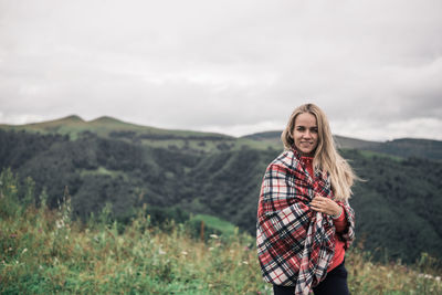 Portrait of smiling woman with blanket standing on mountain against sky