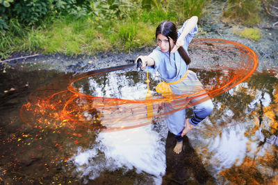 Young woman practicing kung fu with sword while standing on puddle in forest