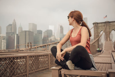 Woman sitting on bridge against sky