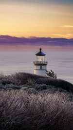 Lighthouse by sea against sky during sunset