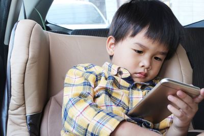 Asian boy looking at smartphone screen. child sitting on car seat and watch cartoon on mobile phone.