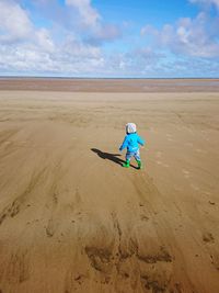 Rear view of kid standing on sand against sea at beach