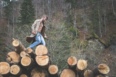 Young man walking on logs of wood in forest 