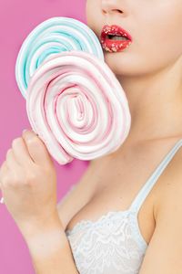 Close-up of woman holding lollipops while standing against pink background