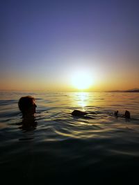Silhouette person swimming in sea against sunset sky