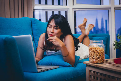 Young woman using mobile phone while sitting on sofa