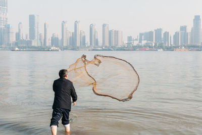 Rear view of man throwing fishing net in yangtze river by city