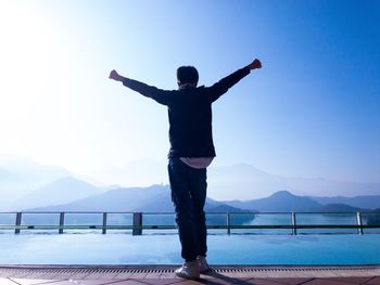 Full length of man with arms outstretched standing against lake in city