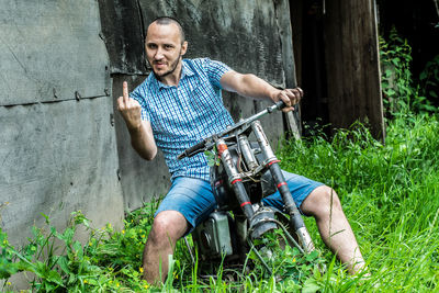 Young man gesturing while sitting on abandoned motorcycle at grassy field