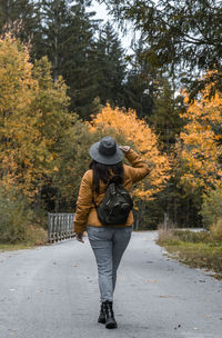 Rear view of woman with backpack, walking on road through autumn woods