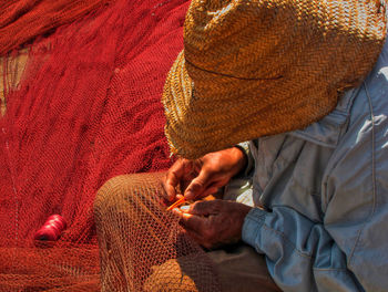 Man sewing fishing net during sunny day