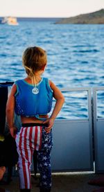 Rear view of boy standing by gate on boat against sky