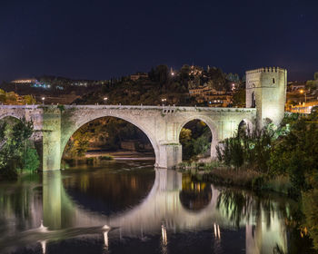 Arch bridge over river against sky at night