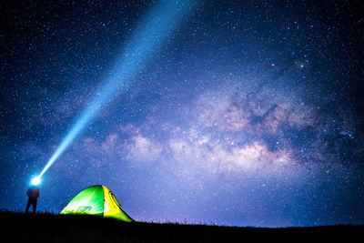 Low angle view of man holding flashlight while standing by tent on field against sky