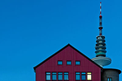 Low angle view of maroon cottage and heinrich-hertz-turm against clear blue sky