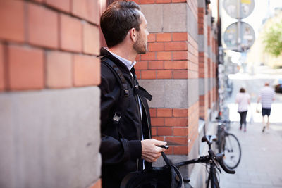 Businessman with helmet looking away while standing by wall in city