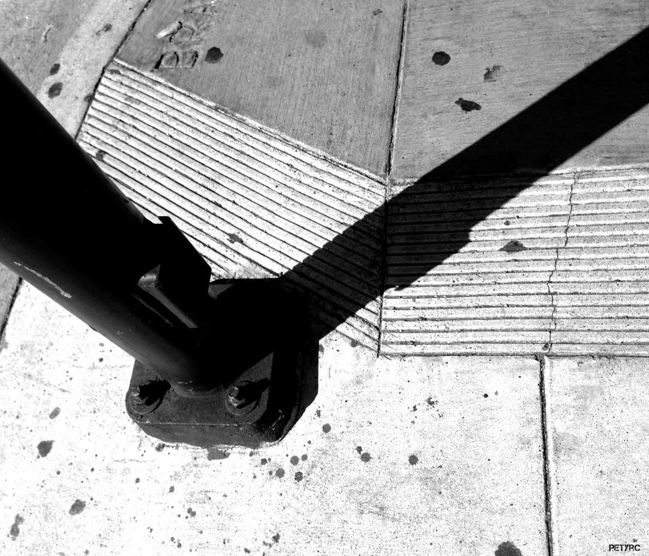 high angle view, shadow, street, metal, sunlight, close-up, sidewalk, day, transportation, outdoors, one person, road, part of, protection, textured, metallic, pattern, wheel, single object, ground