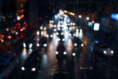 Illuminated vehicles seen through wet window in city at night