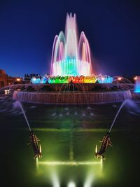 Illuminated fountain in city against sky at night