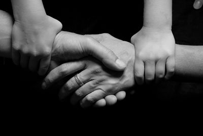 Cropped image of people with holding hands against black background