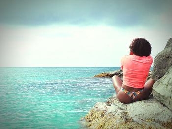 Rear view of woman sitting on rock looking at sea