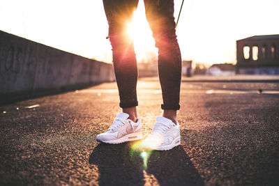 Low section of woman standing on road at sunset