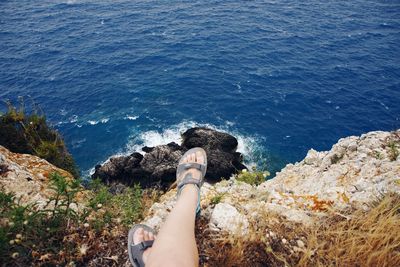 Low section of woman sitting on mountain by sea