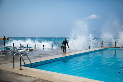 Man swimming in pool by sea against clear blue sky