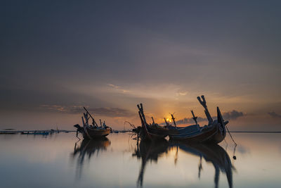 Silhouette boats moored in sea against sky during sunset