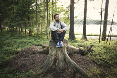 Thoughtful wonderlust man sitting on tree stump in forest