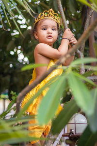 Adorable infant dressed as hindu god krishna cute facial expression playing at tree at janmashtami