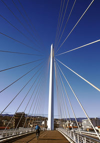 Rear view of young man riding bicycle on suspension bridge against clear blue sky