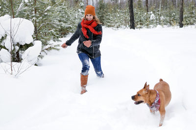 Young woman is playing with her dog on a walk in winter coniferous forest.