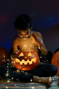 Boy sitting by illuminated pumpkin during halloween