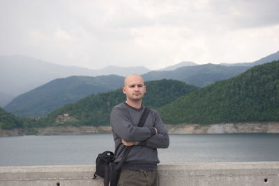 Portrait of bald man with arms crossed standing against mountains