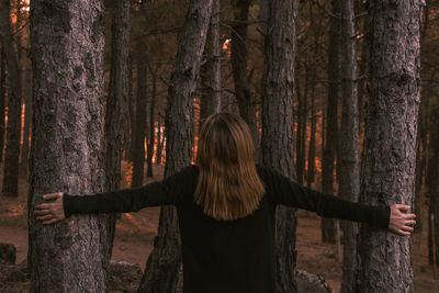 Rear view of woman standing by tree trunk in forest