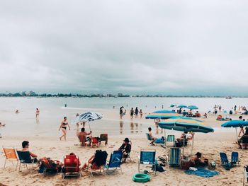 People at beach against cloudy sky