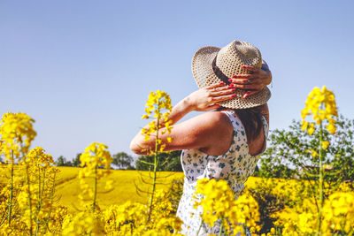Woman wearing hat while standing amidst flowering plants against clear blue sky