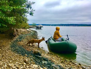 Fox standing by woman on inflatable raft while fishing in lake