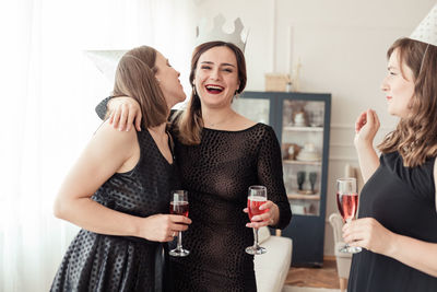 Happy young woman drinking glass while standing at home