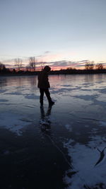 Silhouette man standing on frozen lake during sunset
