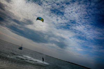 Low angle view of people paragliding against sky