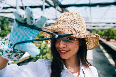 Portrait of smiling young woman holding scissors in greenhouse