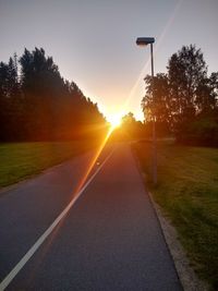 Road by trees against sky during sunset