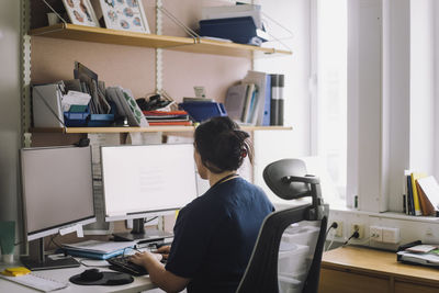 Rear view of mature female nurse working on computer in clinic