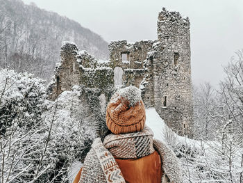 Rear view of young woman in winter clothes looking at castle ruins in winter, snow.