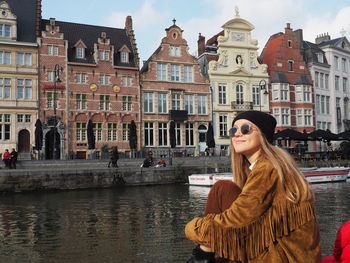 Beautiful woman by canal against buildings in city