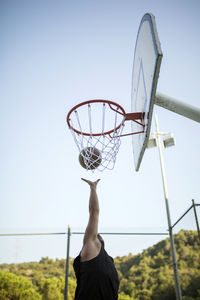 Rear view of man playing basketball against sky