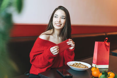 Smiling young woman holding drink sitting on table